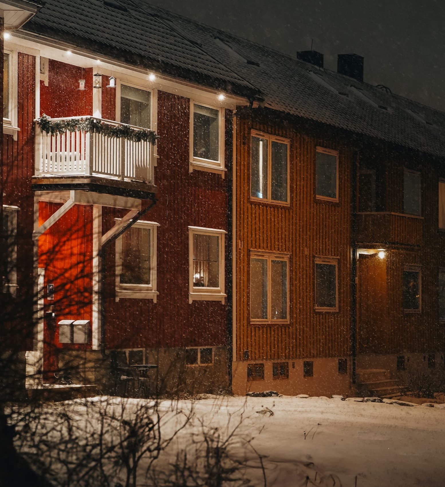 Svenska flerbostadshus en vinterkväll, med ljus i fönstren och snöfall